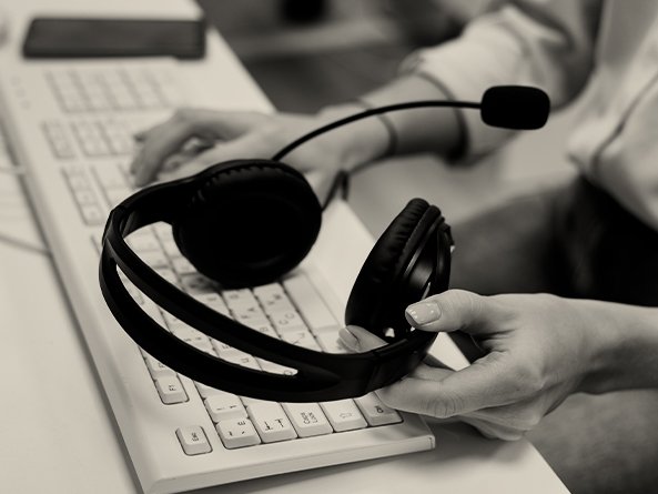 Canal do Cliente - Pessoa digitando em teclado com uma das mãos e segurando um headphone com a outra mão