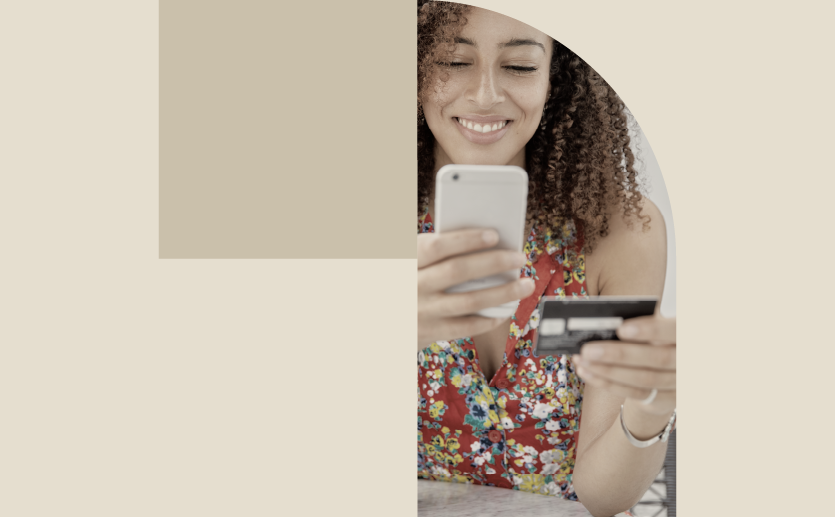 Mulher jovem segura um cartão de crédito e um celular nas mãos.